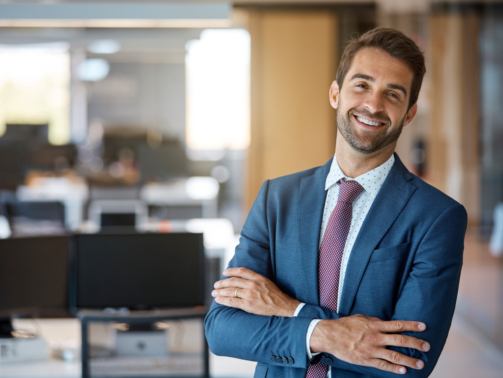 Portrait of smiling businessman standing with arms crossed. Confident male professional is in office. He is wearing suit.