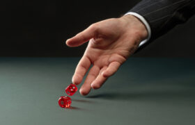 caucasian hand rolling two red dice representing how pharmacy benefit costs are risky.