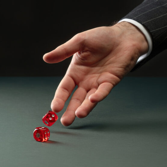 caucasian hand rolling two red dice representing how pharmacy benefit costs are risky.