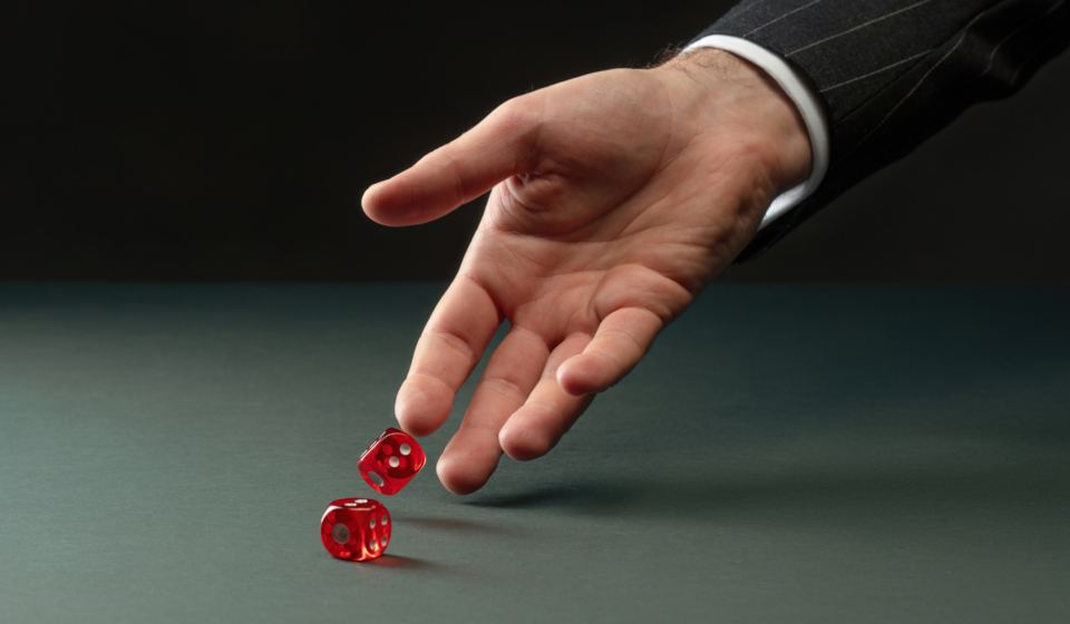 caucasian hand rolling two red dice representing how pharmacy benefit costs are risky.