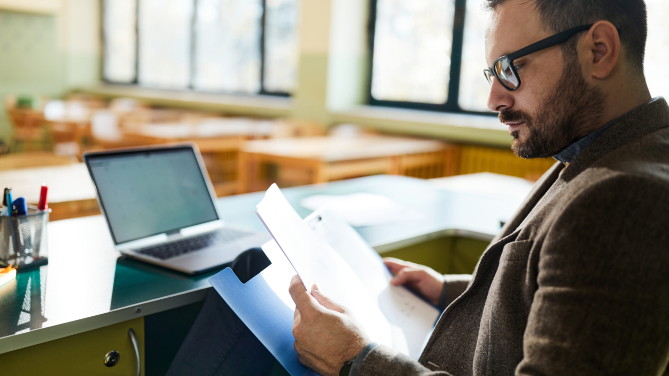 Male teacher reading paperwork in classroom.