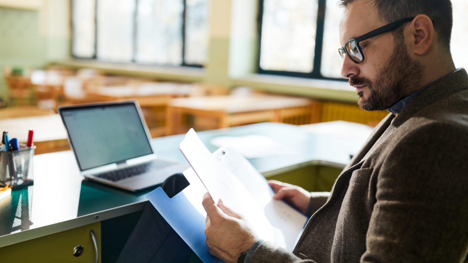 Male teacher reading paperwork in classroom.