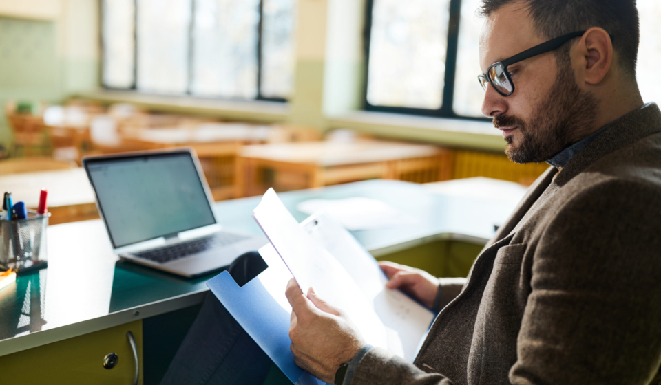 Male teacher reading paperwork in classroom.